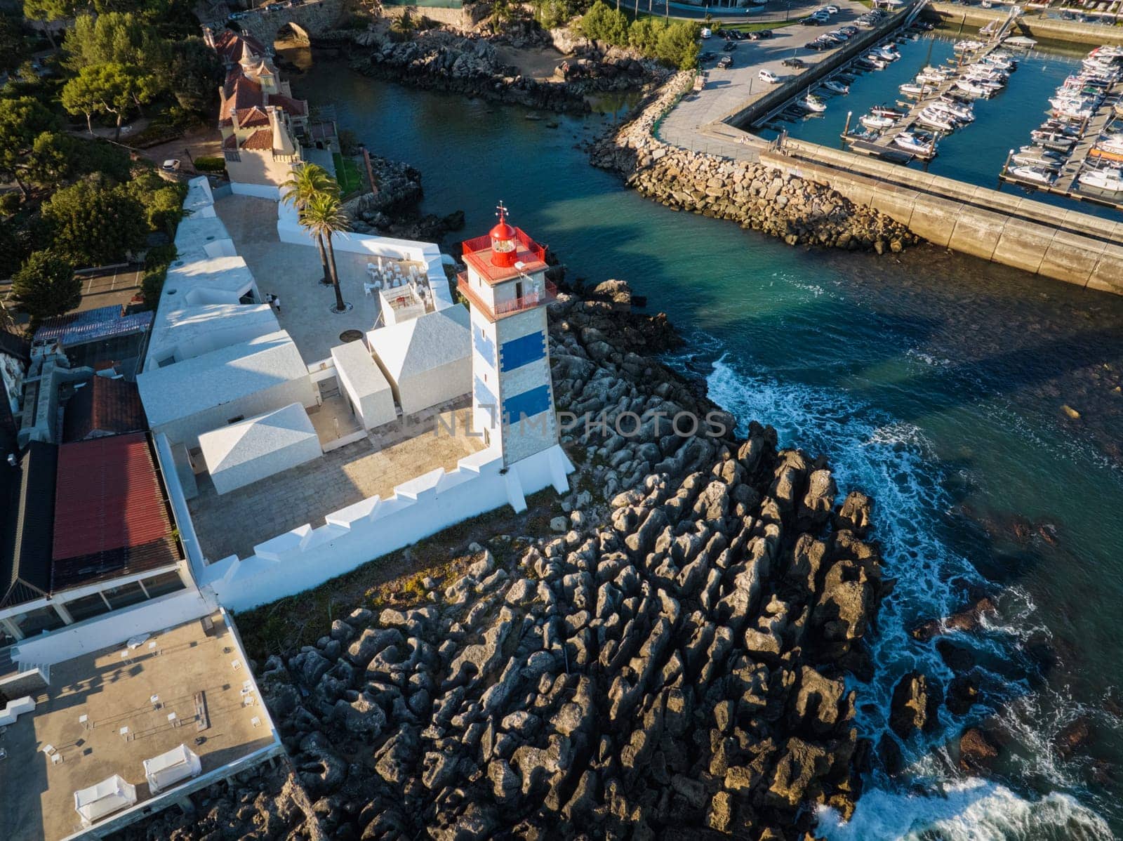 Aerial view of Santa Marta lighthouse and Cascais marina with moored yacht boats with Cascais cityscape, Portugal on sunset