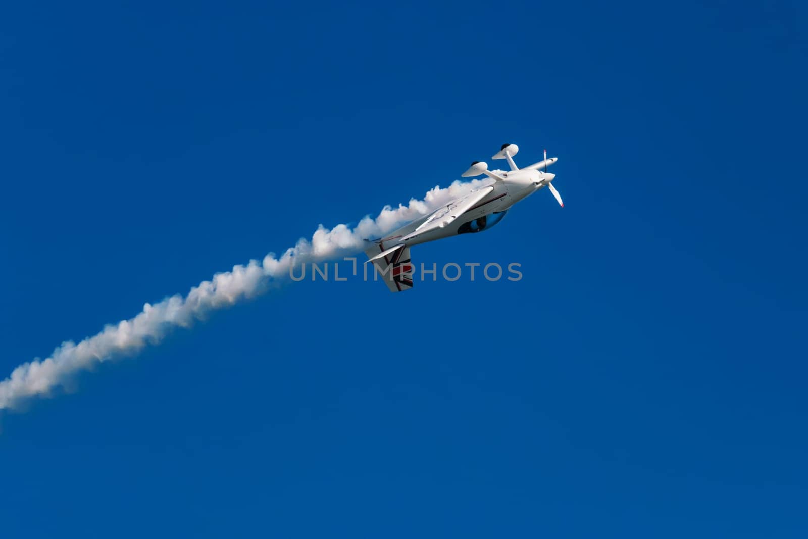 Stunt aerobatic plane performing stunts in blue sky with smoke trail. Concept of speed, difficulty, precision, risk, challenge