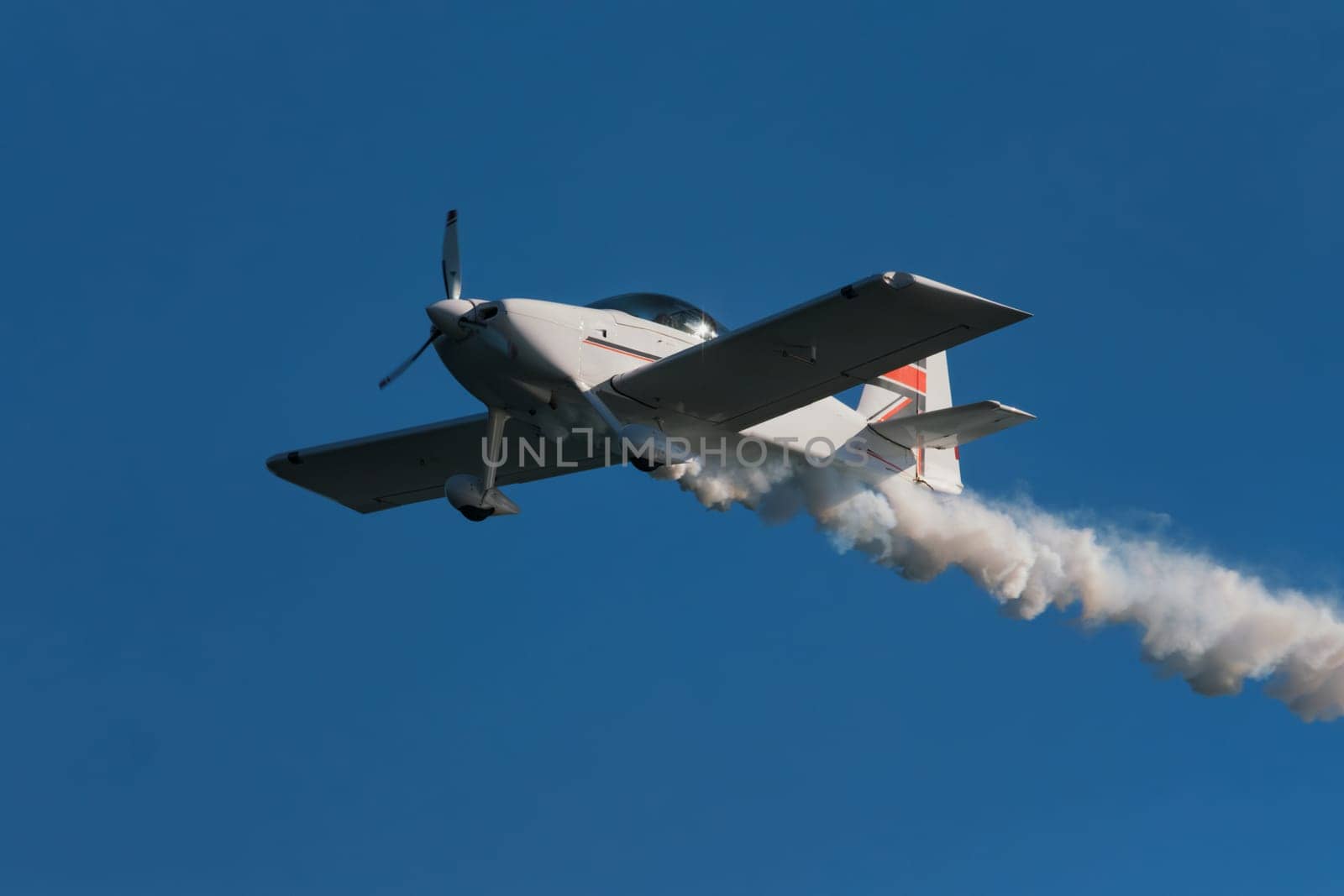 Stunt aerobatic plane performing stunts in blue sky with smoke trail. Concept of speed, difficulty, precision, risk, challenge
