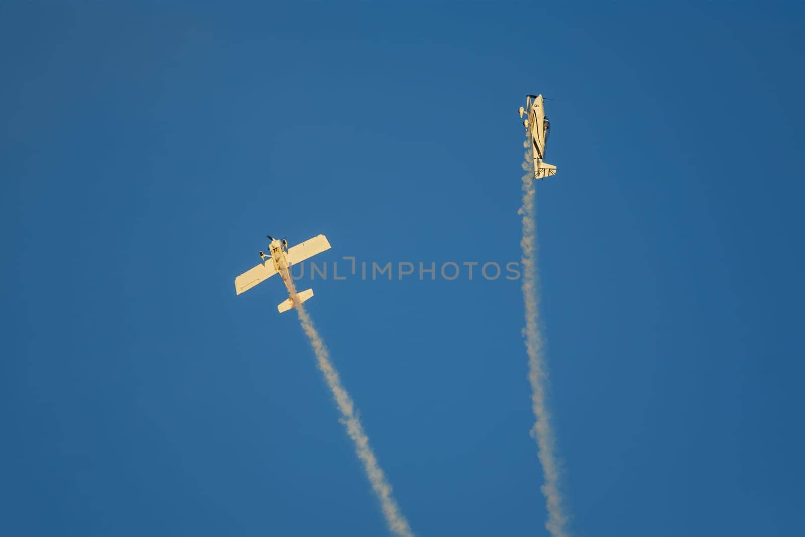 Stunt aerobatic plane performing stunts in blue sky with smoke trail. Concept of teamwork, collaboration, coordination, trust, precision, difficulty, challenge, speed, synergy