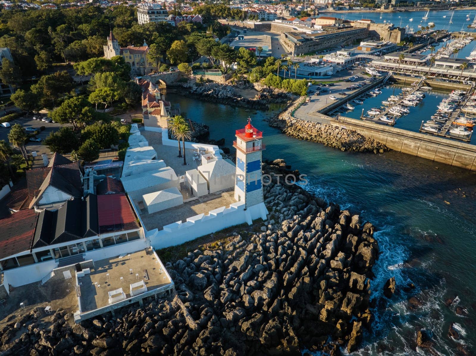 Aerial view of Santa Marta lighthouse and Cascais marina with moored yacht boats with Cascais cityscape, Portugal on sunset
