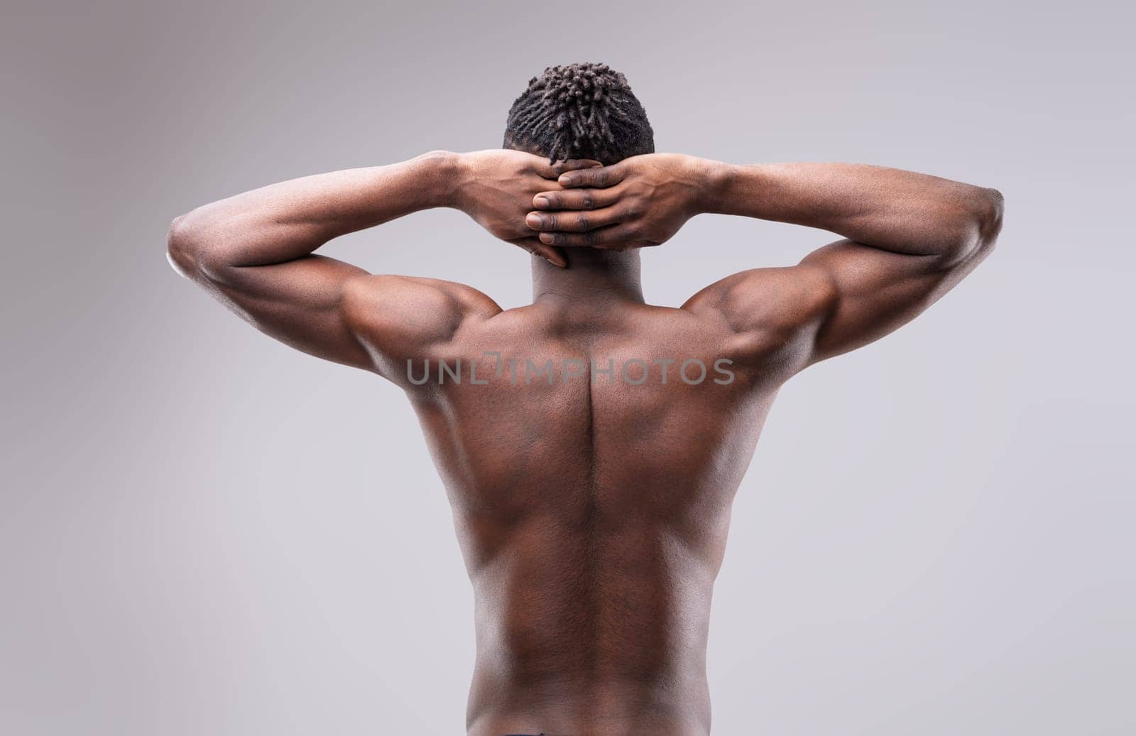 Shirtless sportsman posing with hands behind his head, highlighting strong back and arms while confidently gazing at the camera, exuding power and determination