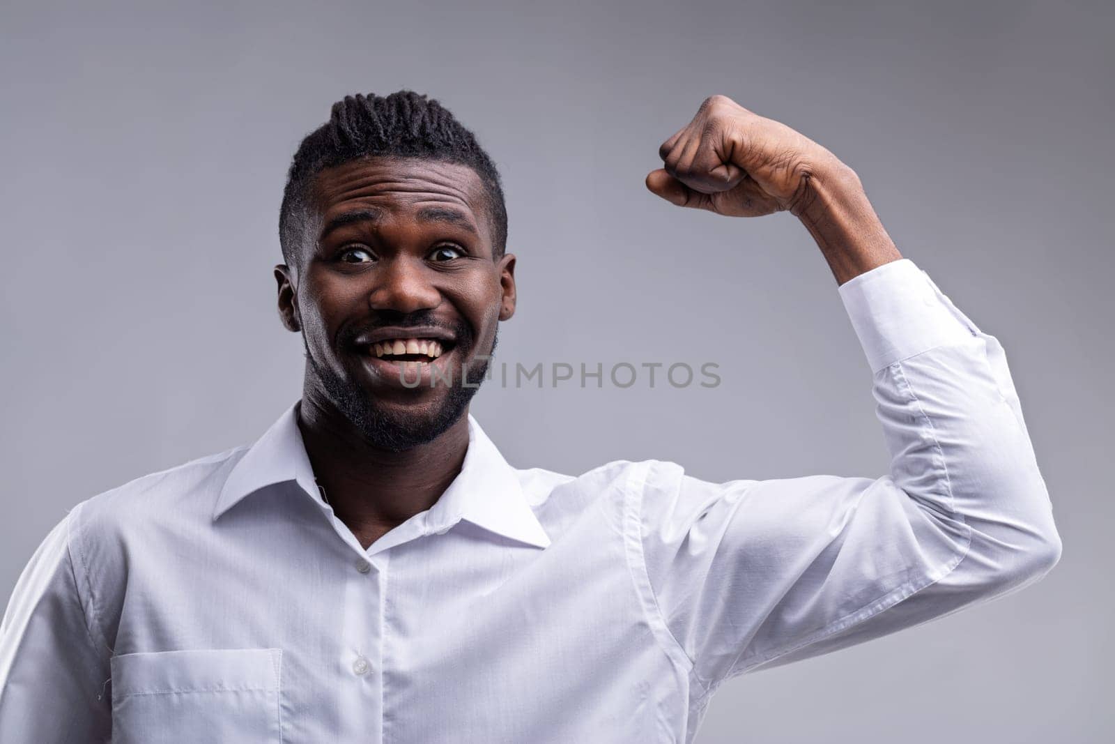 Excited young adult businessman flexing his bicep and smiling at the camera, showing his strength and determination on a neutral background