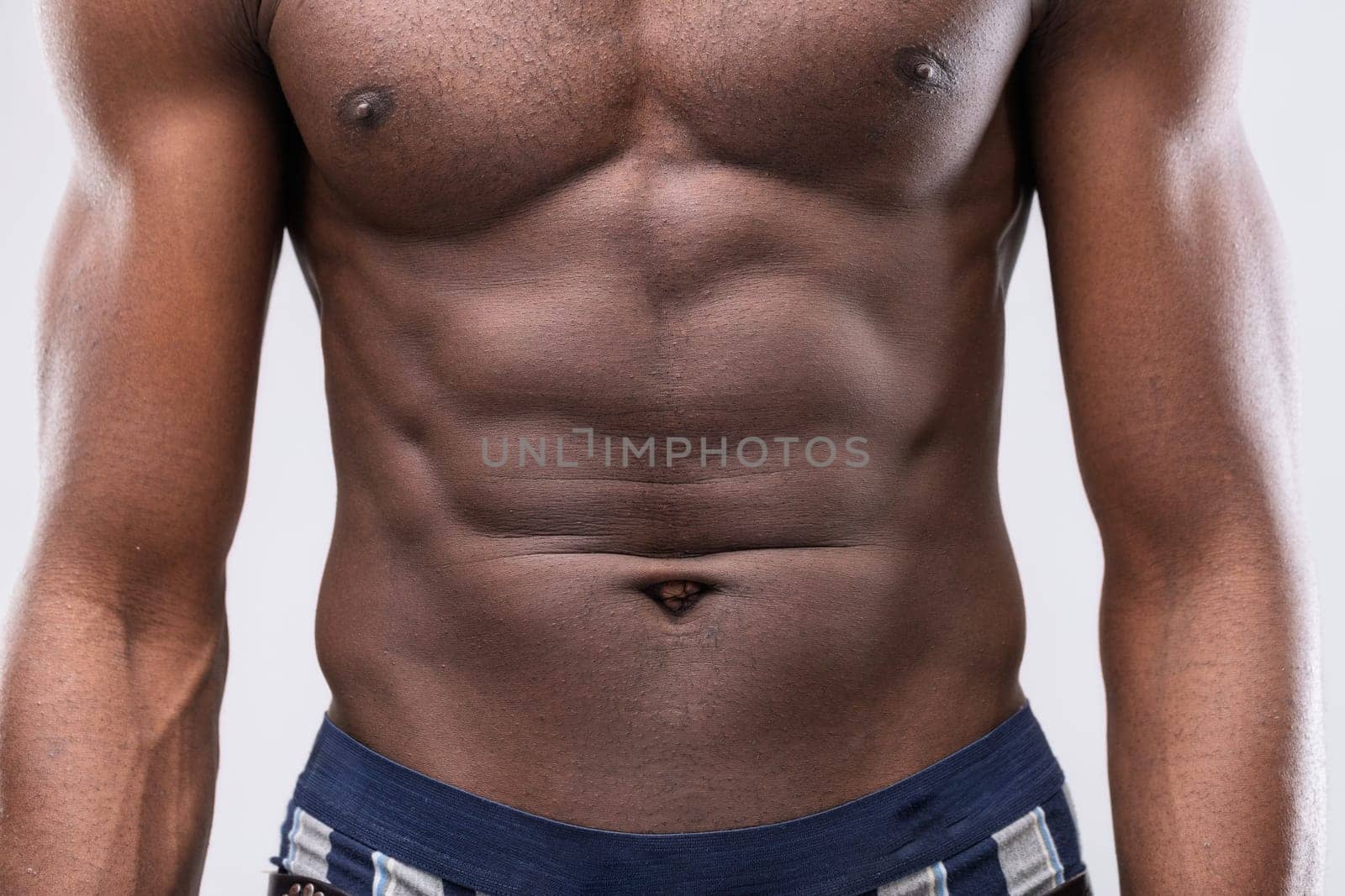 Close-up view of a shirtless, muscular black man proudly displaying his well-defined abs and chest, highlighting his dedication to fitness and showcasing his impressive physique