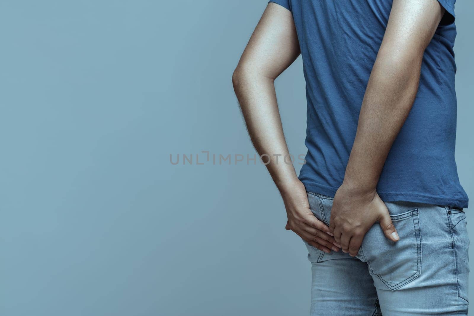 Man holding his bottom with both hands, experiencing discomfort from hemorrhoids, anal pain, and constipation, set against a soft gradient background