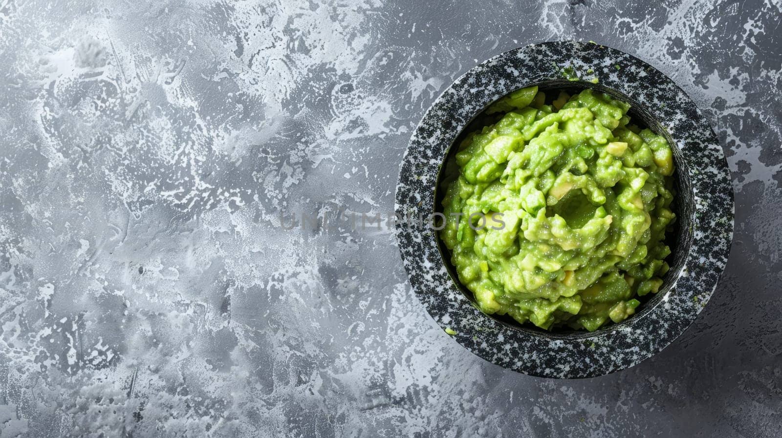 Artisanal guacamole seasoned with spices, garnished with cilantro beside a ripe avocado, combining tradition with gourmet appeal. The dark mortar sets off the green hues vividly