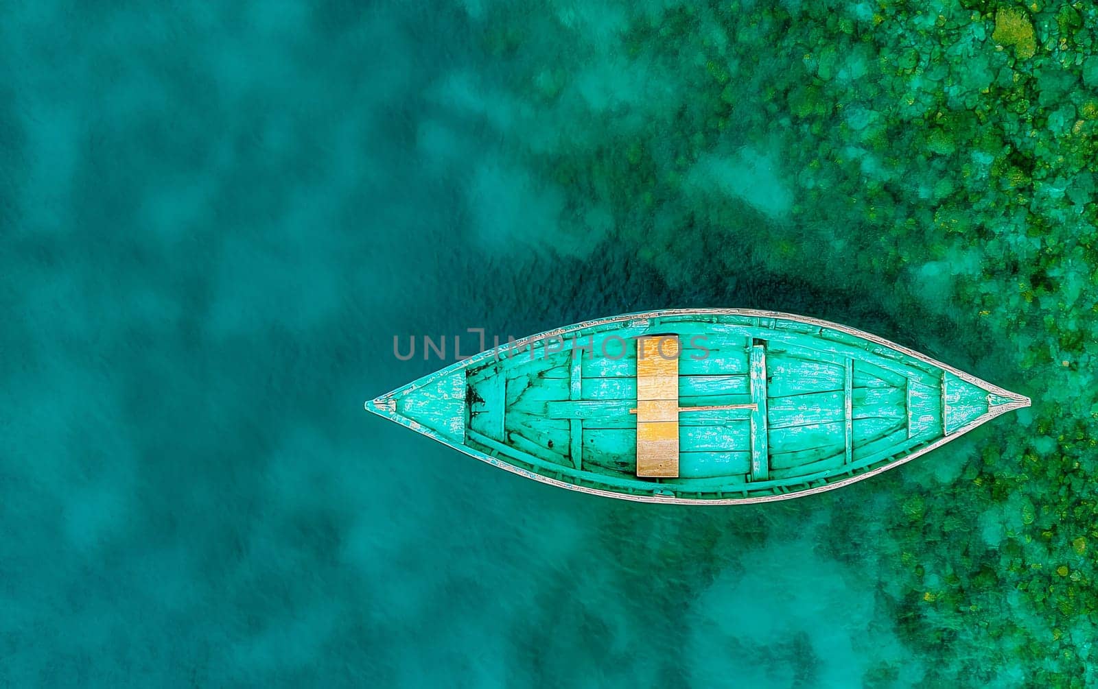 Aerial view of turquoise wooden boat on vibrant teal water surface.