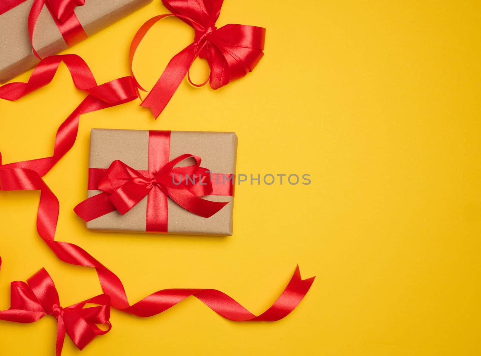 Two boxes tied with red ribbon on yellow background, festive background.