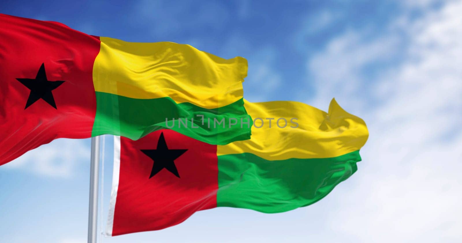 National flags of Guinea-Bissau waving in the wind on a clear day. Vertical red stripe, black star left, yellow and green horizontal stripes right. 3d illustration render. Fluttering fabric