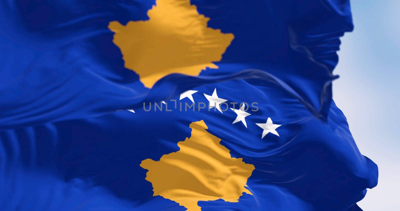 Close-up of Kosovo national flags waving on a clear day. Six white stars above a golden map of Kosovo in a blue field. 3d illustration render. Rippling textured fabric.