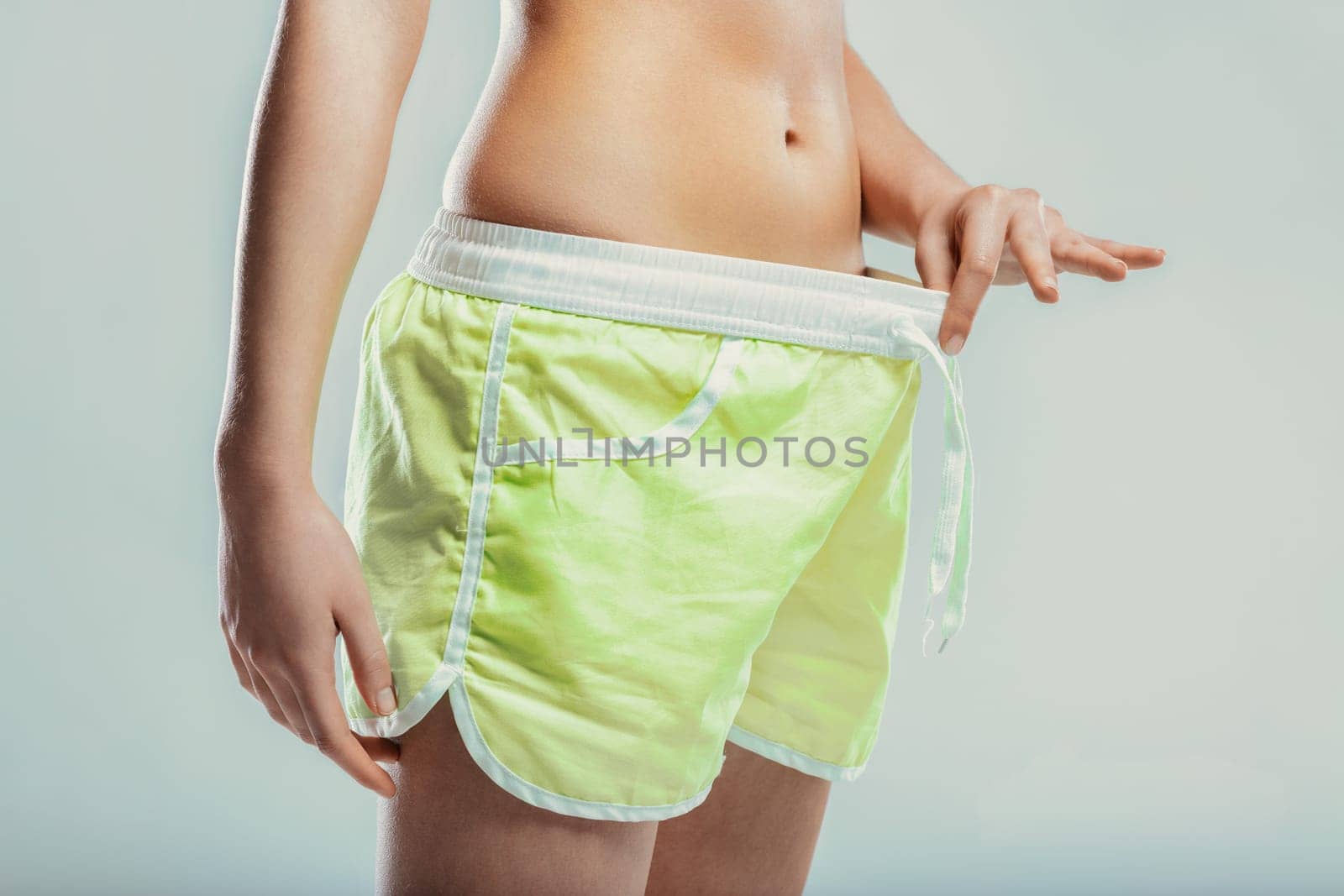 Young slim woman pulling down her shorts, celebrating weight loss progress and embodying the concepts of liposuction and tummy tuck, radiating confidence and determination