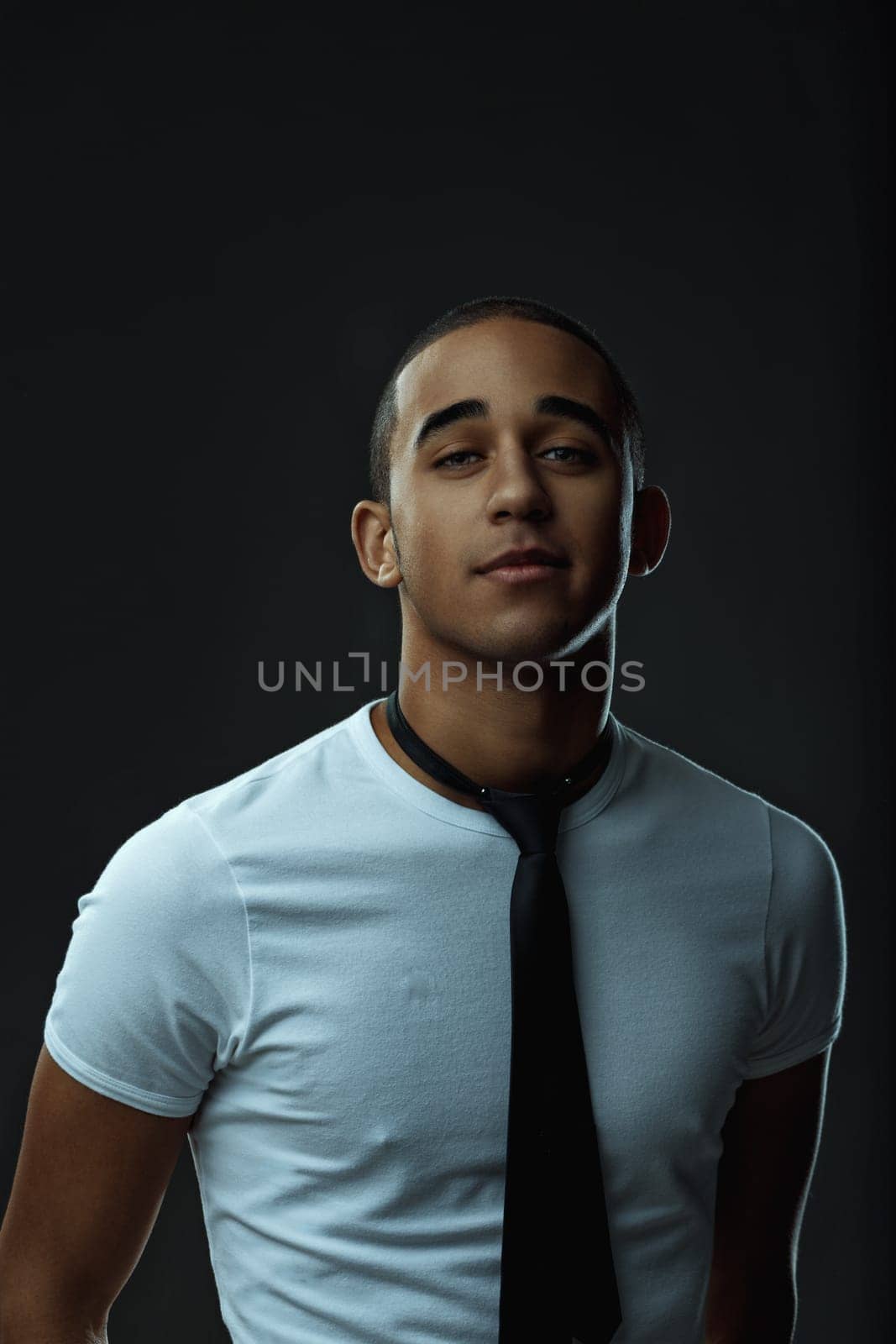 Portrait showcasing a stylish young man in a tie, confidently looking at the camera against a sleek black background. Portrait