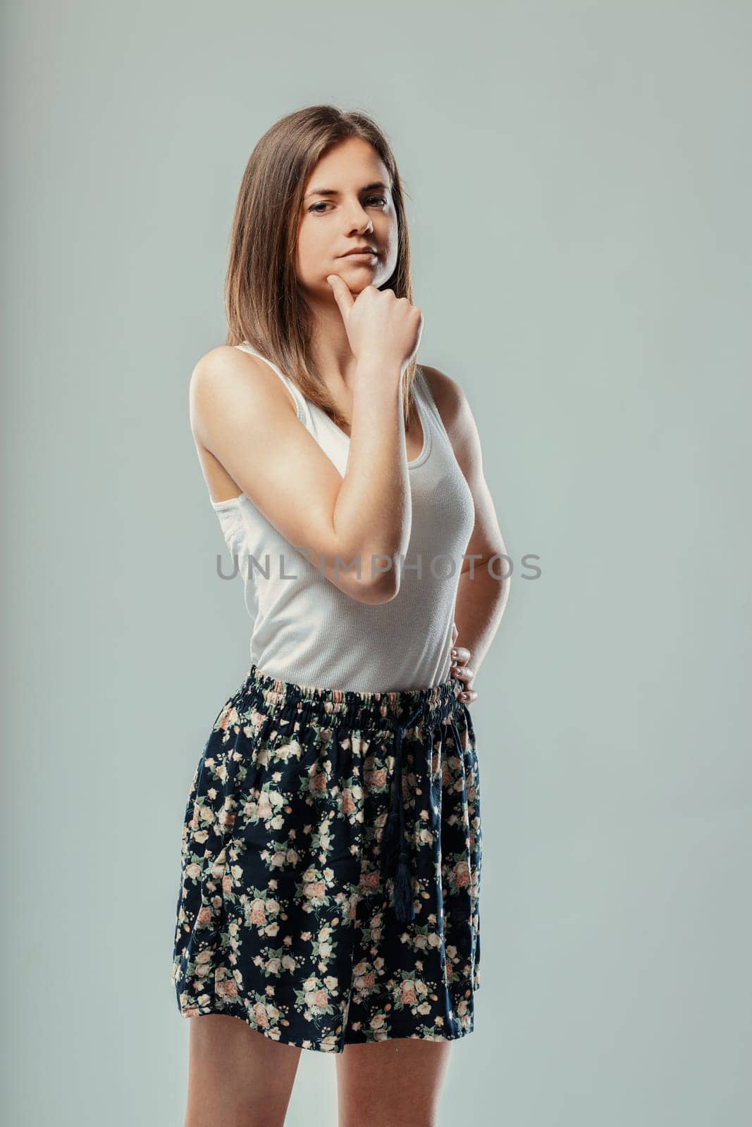 Portrait of a thoughtful young woman touching her chin with her hand, expressing deep thought and contemplation against a neutral gray background