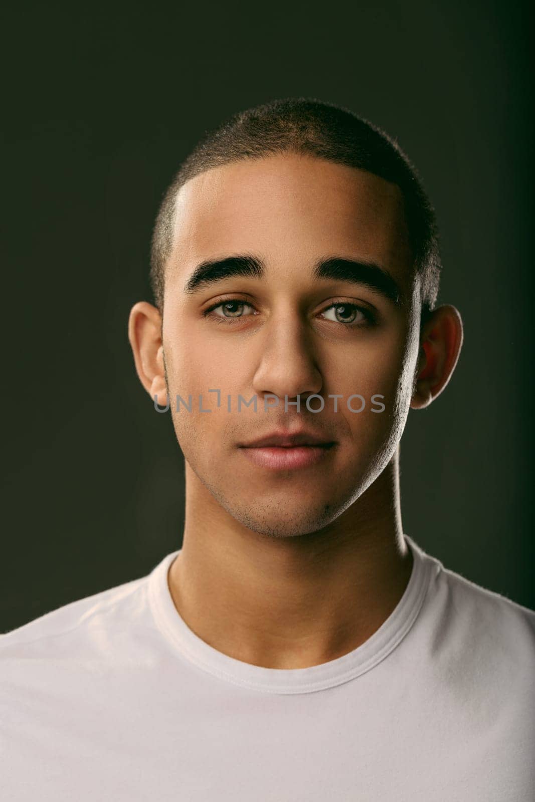Serious young man gazing directly at the camera against a dark background, exuding calm confidence and deep contemplation. Portrait