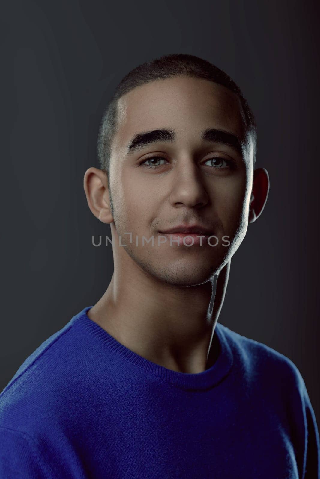 Portrait of a handsome young man wearing a blue sweater, smiling and looking at the camera on a gray background. Portrait