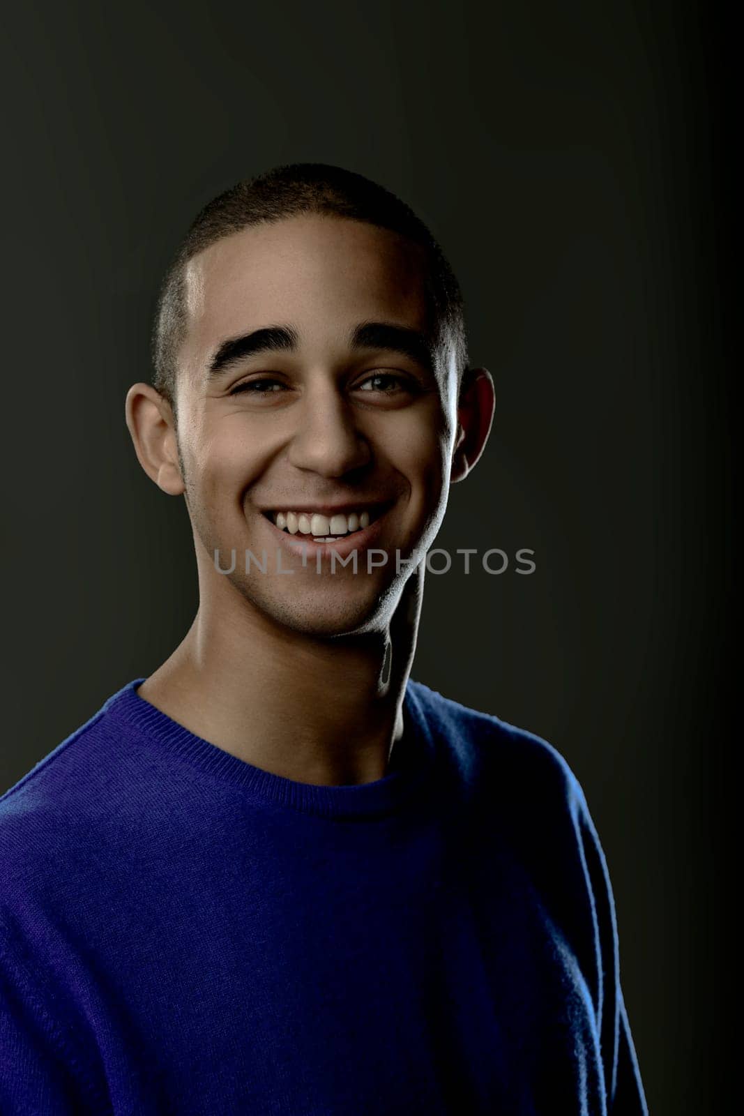 Portrait of a cheerful young man smiling and looking at the camera against a dark background. Portrait