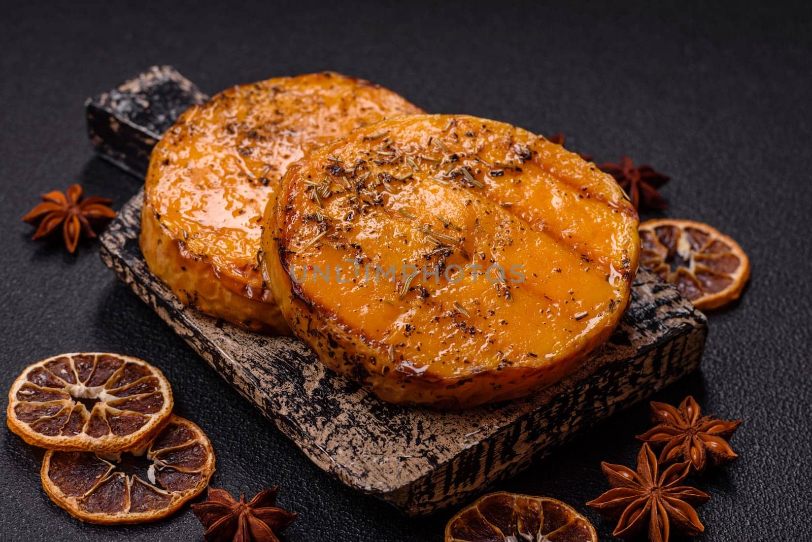 Pumpkin cut into slices and grilled with rosemary and spices on a dark concrete background