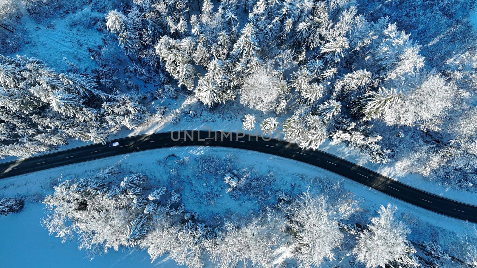 Drone shot of a winding road in winter with a car