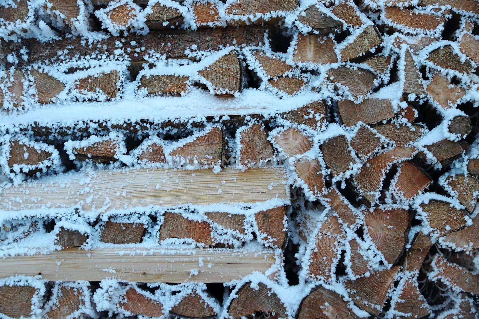 A pile of firewood with snow and hoarfrost in winter