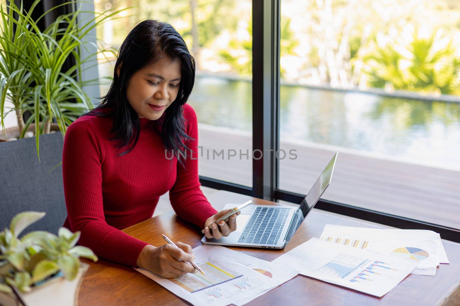 Busness women wearing red sweater working about new startup on smartphone to analysis finance of project in outside office, Woman working using laptop online meeting in home office.