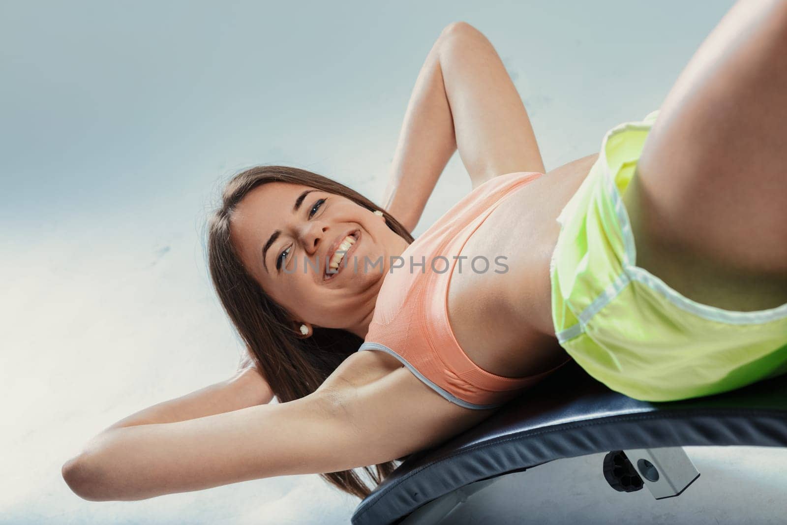 Happy sportswoman training her abs while performing crunches and smiling at the gym, radiating positivity and determination in a vibrant, energetic environment