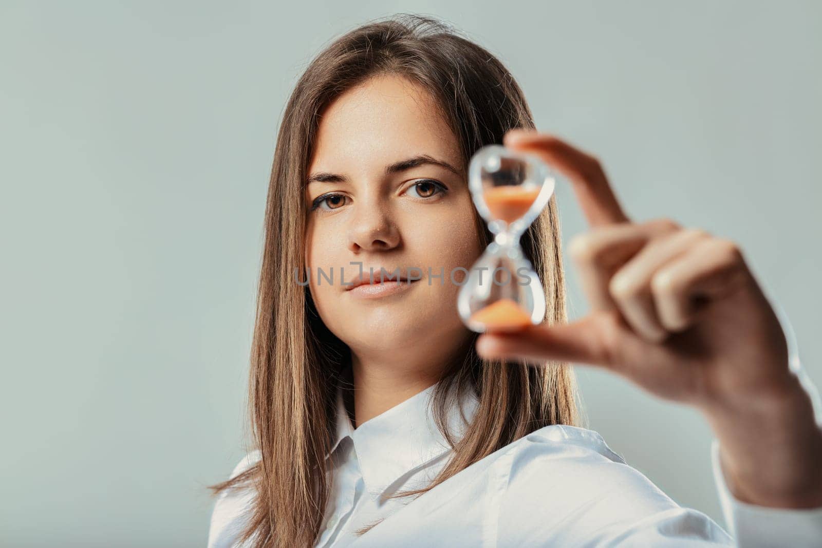 Young businesswoman looking at camera and showing an hourglass, symbolizing time management, efficiency, and the passage of time in a professional context