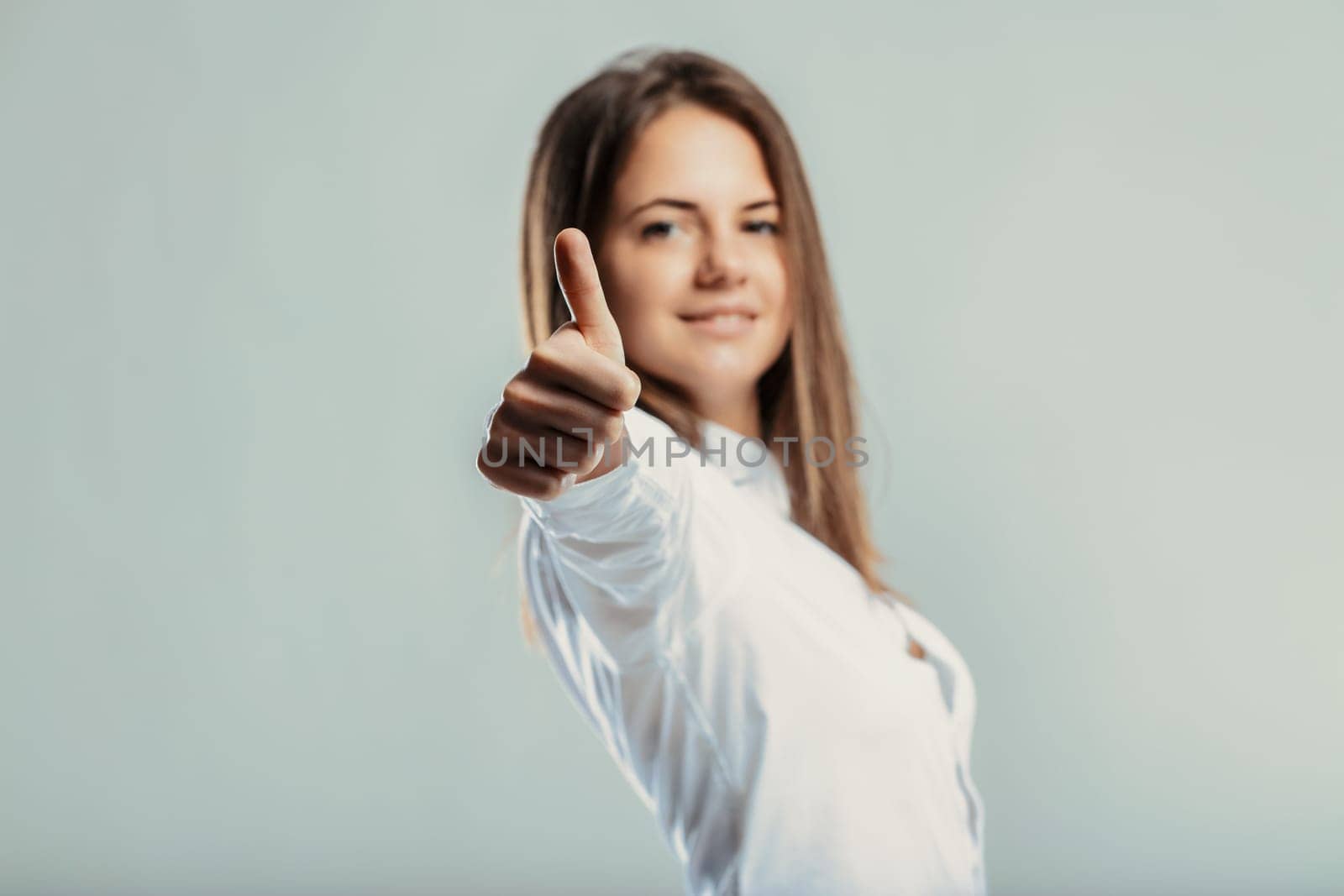 Young businesswoman giving a thumbs up, expressing approval and support while looking confidently at the camera with a bright smile, radiating positivity in a studio setting