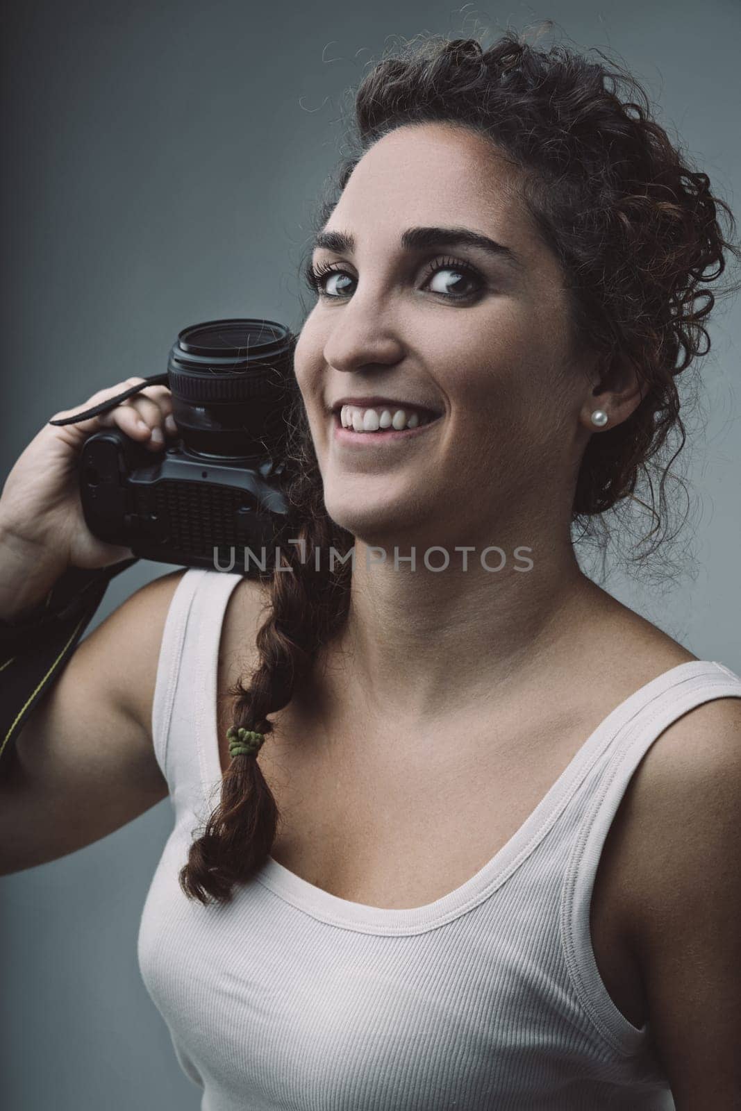 Cheerful young woman photographer holding a dslr camera on her shoulder, radiating passion for photography while capturing moments and expressing her creativity with confidence