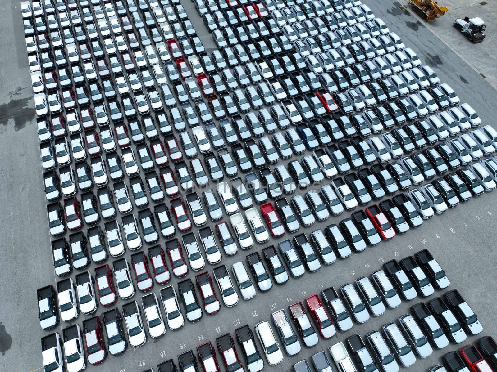 Aerial view of new cars stock at factory parking lot. Above view cars parked in a row. Automotive industry. Logistics business. Import or export new cars at warehouse. Big parking lot at port terminal
