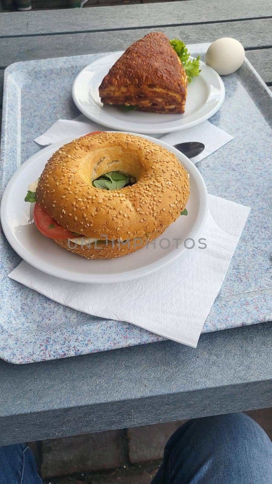 A hearty breakfast spread featuring a sesame seed bagel with tomato and mozzarella, a flaky pastry, and a hard-boiled egg.