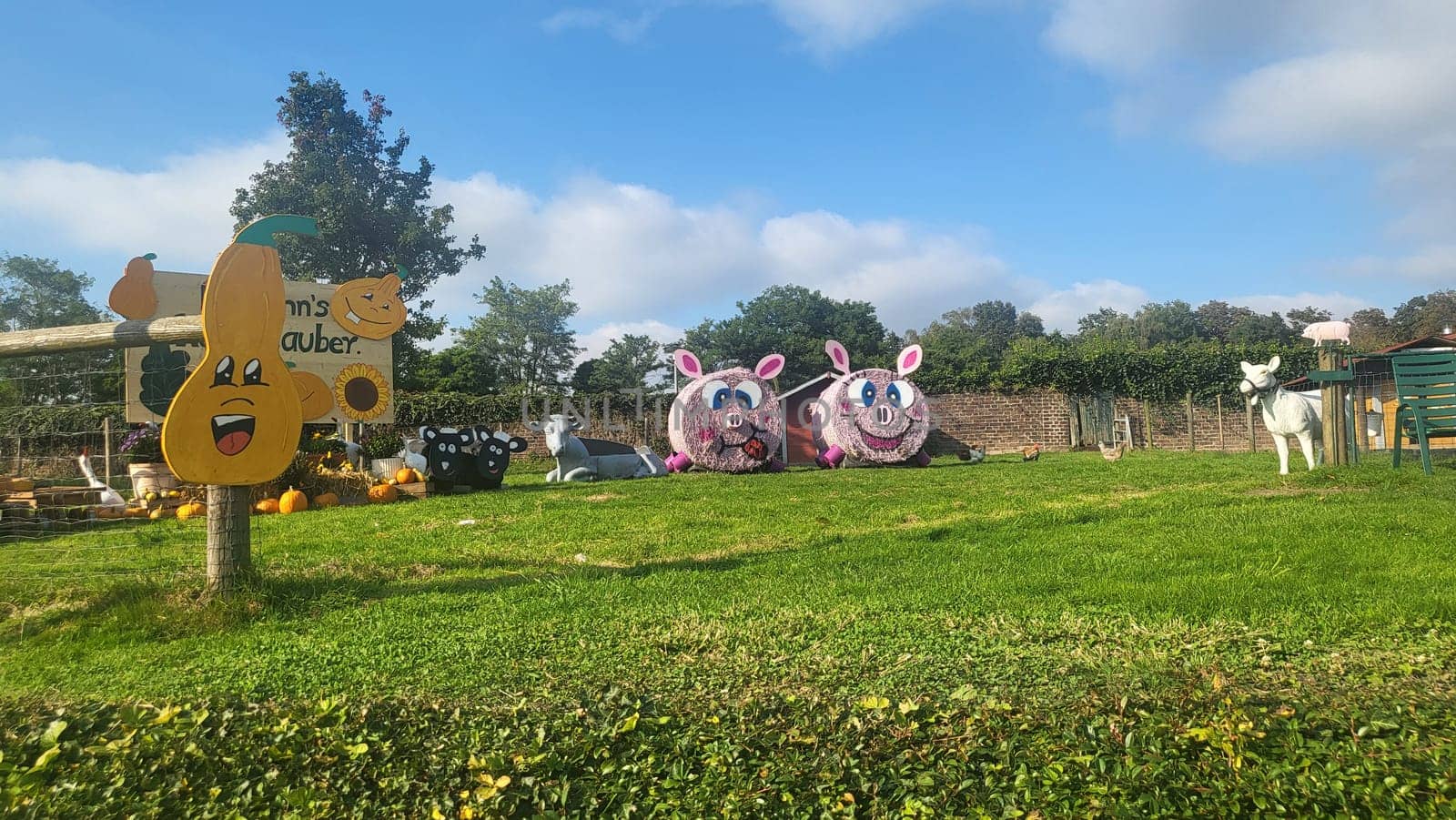 A picturesque farm scene with hay bale pigs, pumpkins, and a sign welcoming visitors.