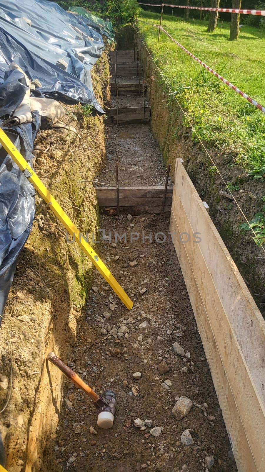 A construction site showing the early stages of foundation work. Exposed earth, wooden formwork, and a level are visible.