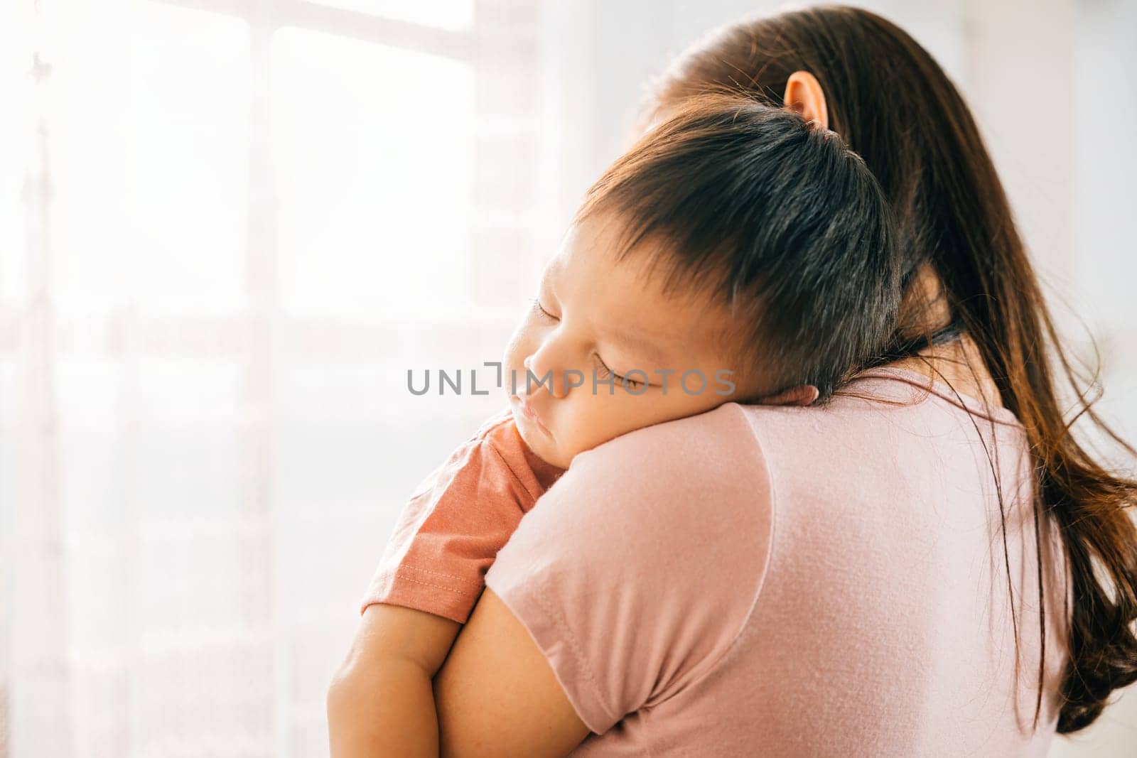 A tender loving biracial mother cradles her small sleeping newborn in her arms sharing an affectionate family moment that exudes the awe of childbirth and the innocence of childhood.