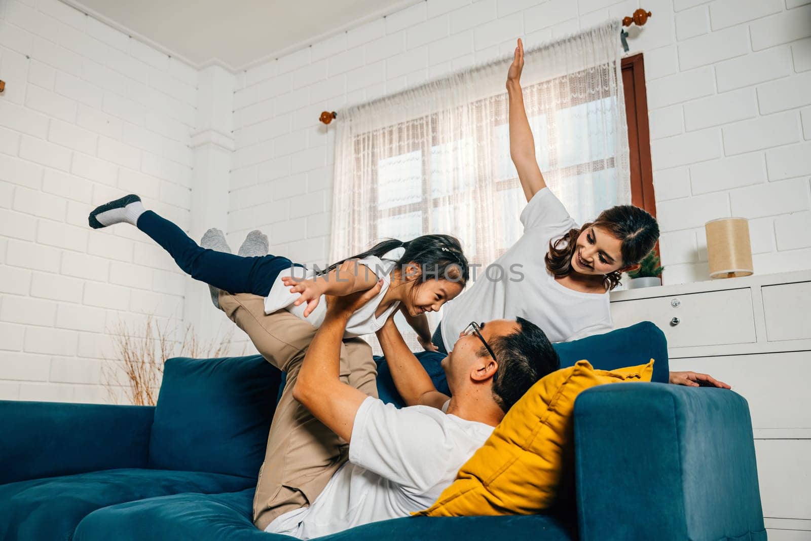 Family fun takes flight in the living room with an airplane game. The child held high on the father's shoulders and supported by the mother enjoys a cheerful carefree time.