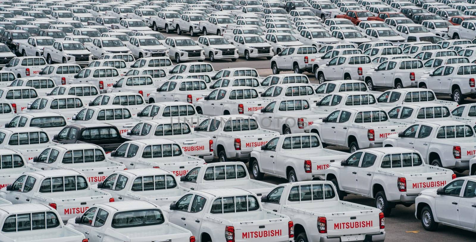 Lamchabang, Thailand - July 02, 2023 bustling car factory distribution center on a cloudy day, new sedans are ready for transport. top view offers glimpse of the crowded parkingan industry in motion.