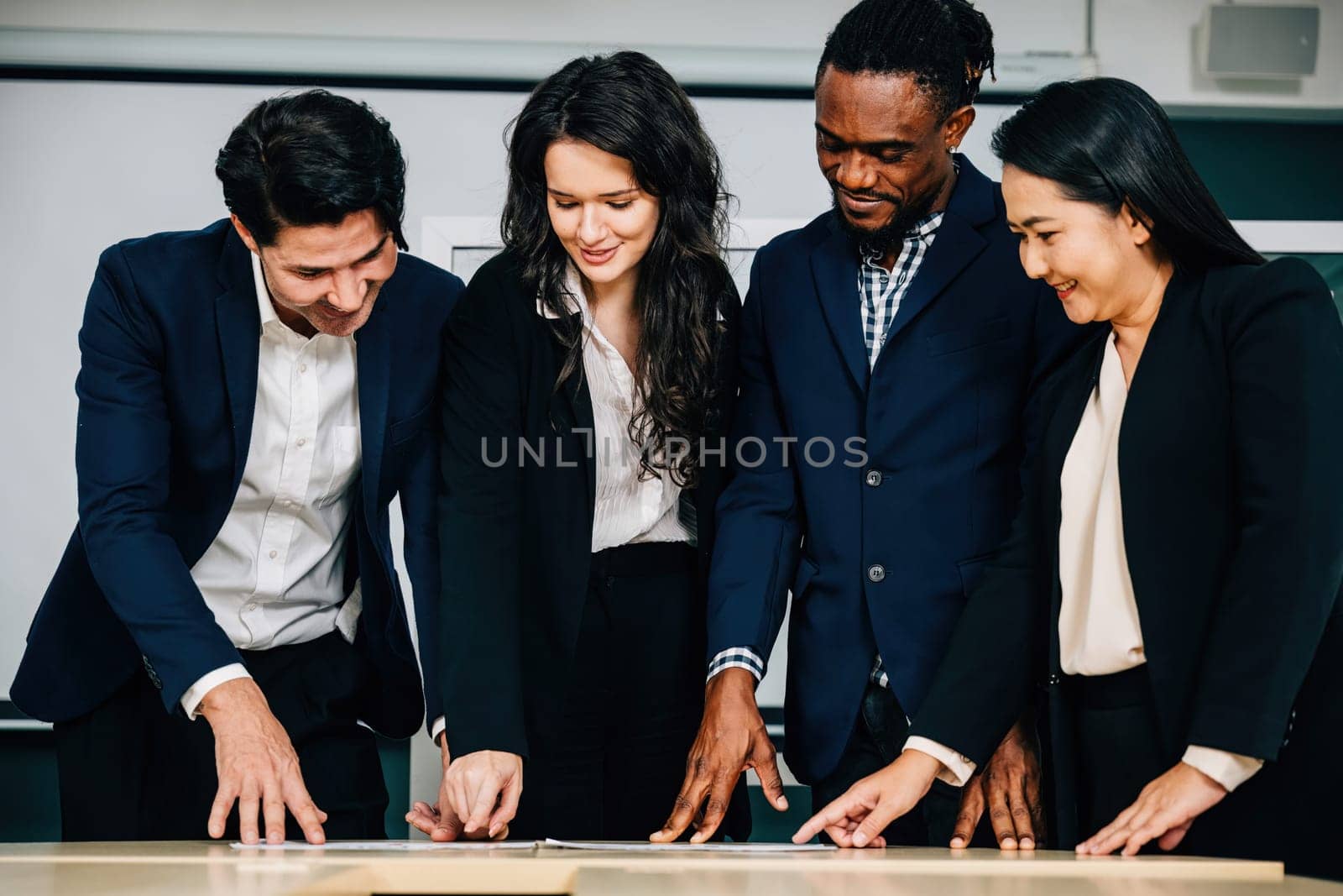 Diverse colleagues stand at a conference room desk, actively participating in a successful meeting. Their teamwork, strategic planning, and cooperation drive business success.