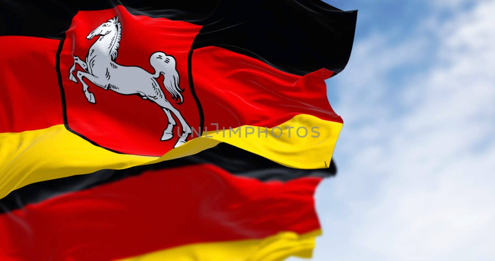 Lower Saxony state flag waving with German flag on a clear day. Black, red and yellow stripes with coat of arms in the center. German state. 3D illustration render. Rippling fabric. Selective focus