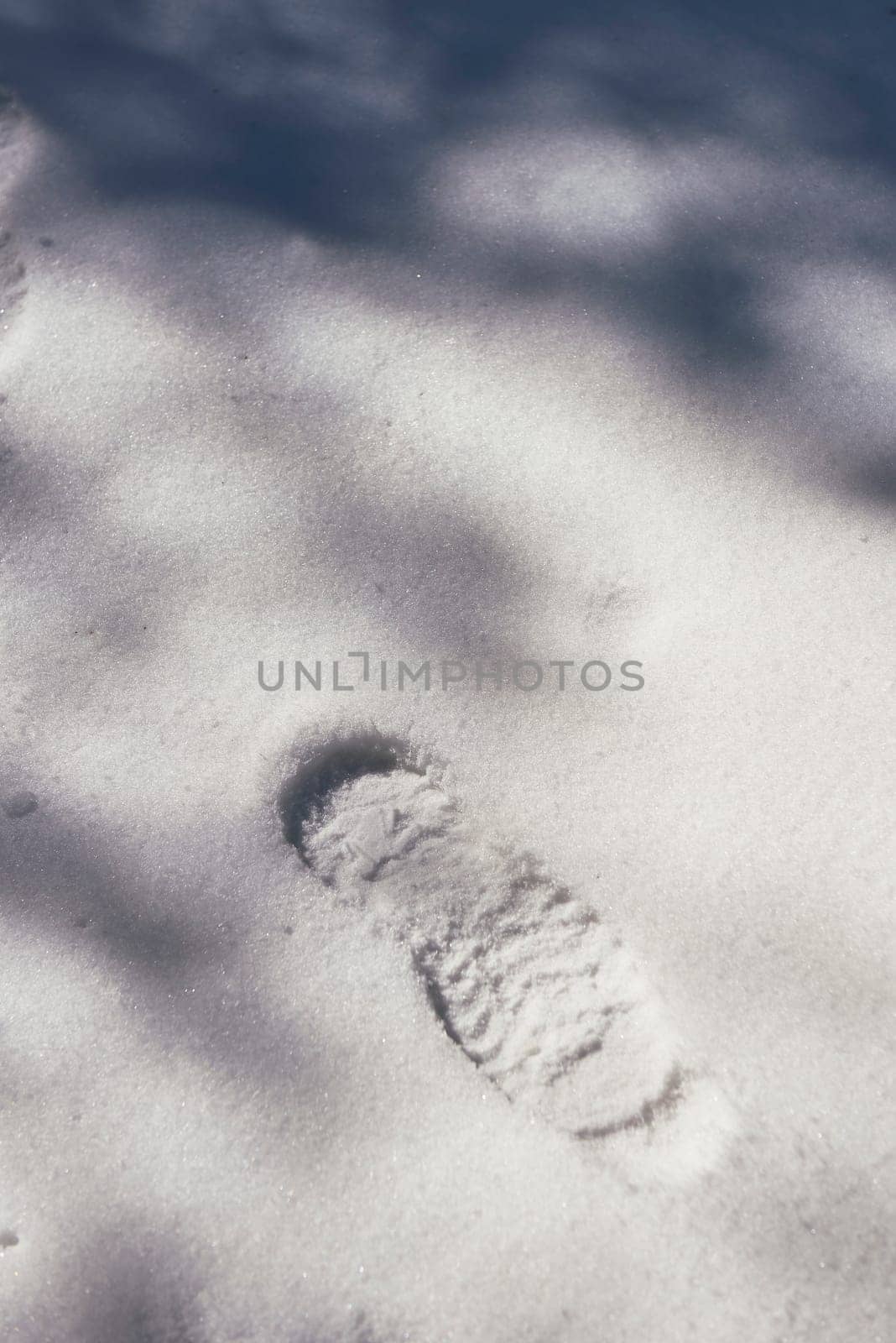 A footprint on virgin snow in sunshine and shadows. Front view, solitary, empty space