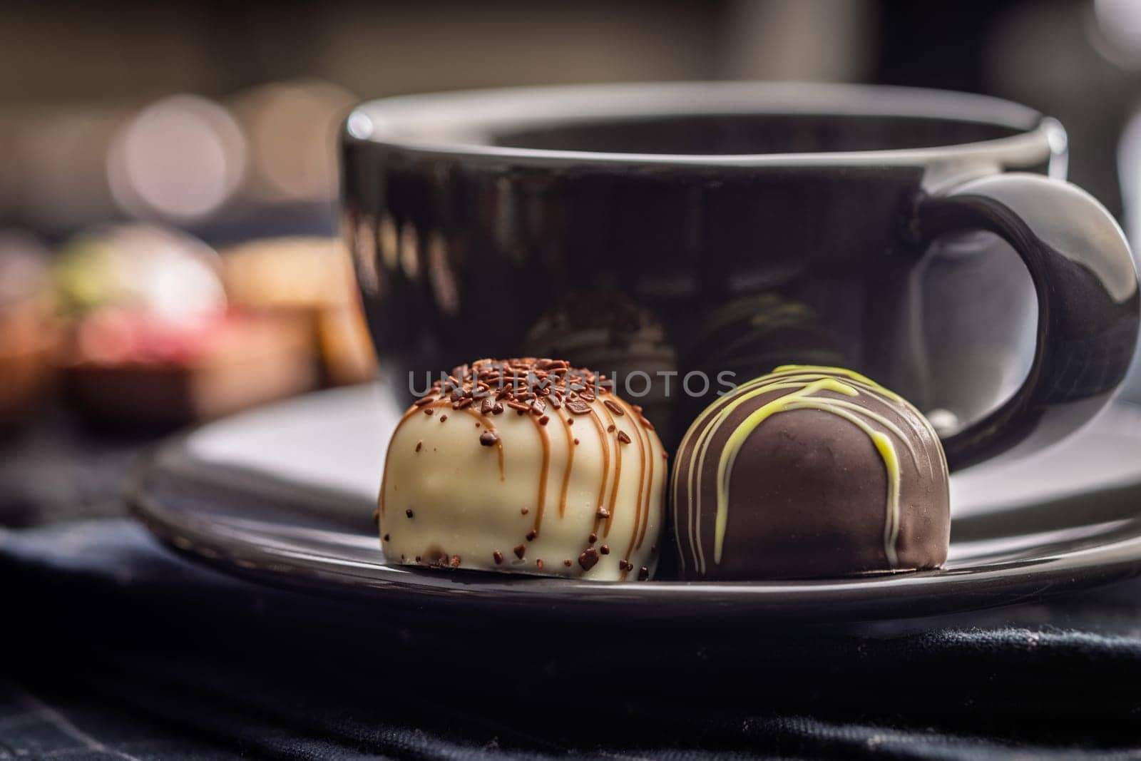 Two chocolate pralines and coffee cup on a black table.