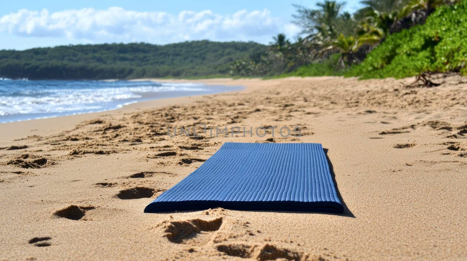 A blue yoga mat laid out on a sandy beach with footprints leading to it, surrounded by lush greenery and ocean waves under a bright sky.