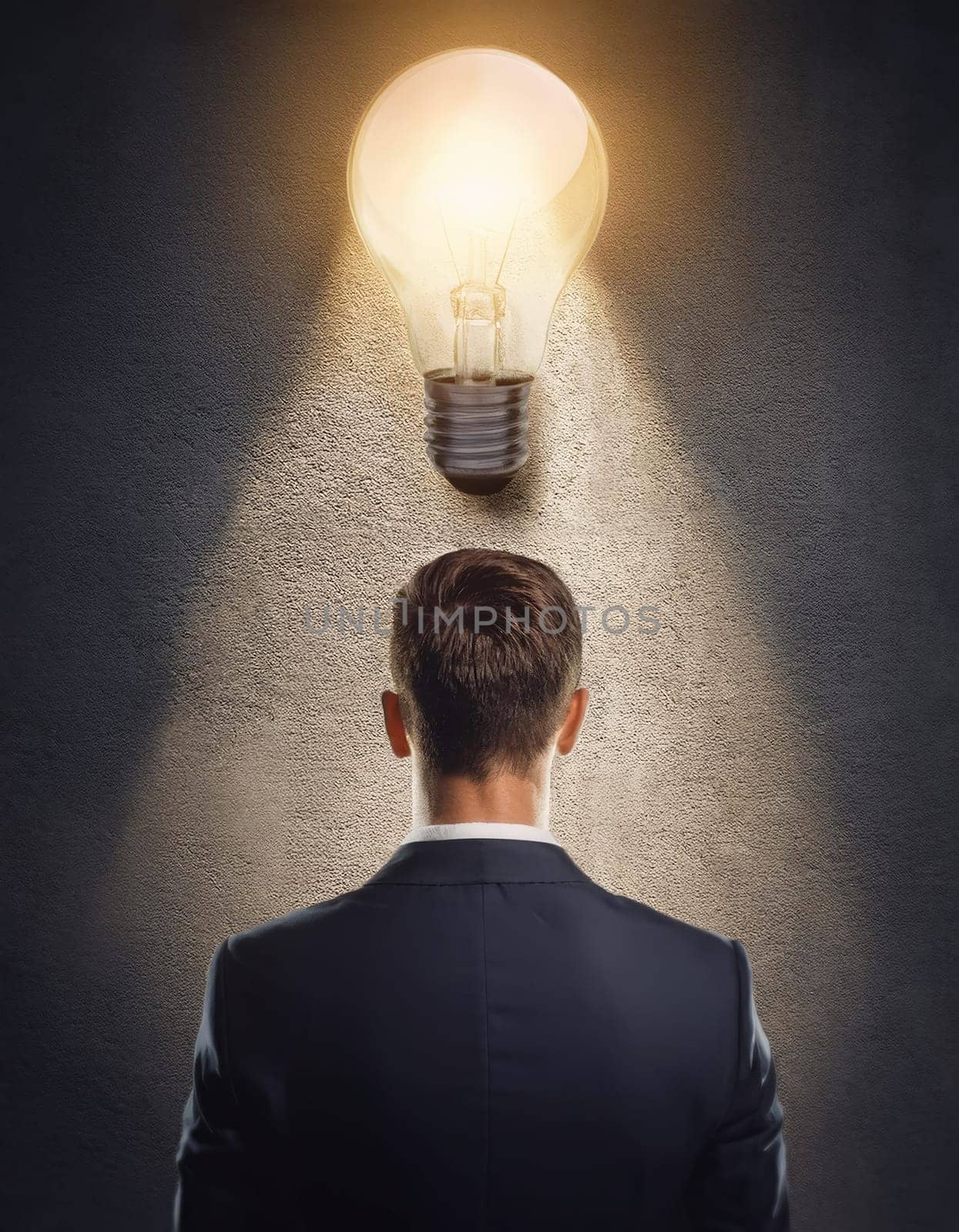 Closeup rear view thoughtful businessman inside a dark room with a glowing lightbulb above head. Bulb as symbol for genius idea, inspiration and creativity
