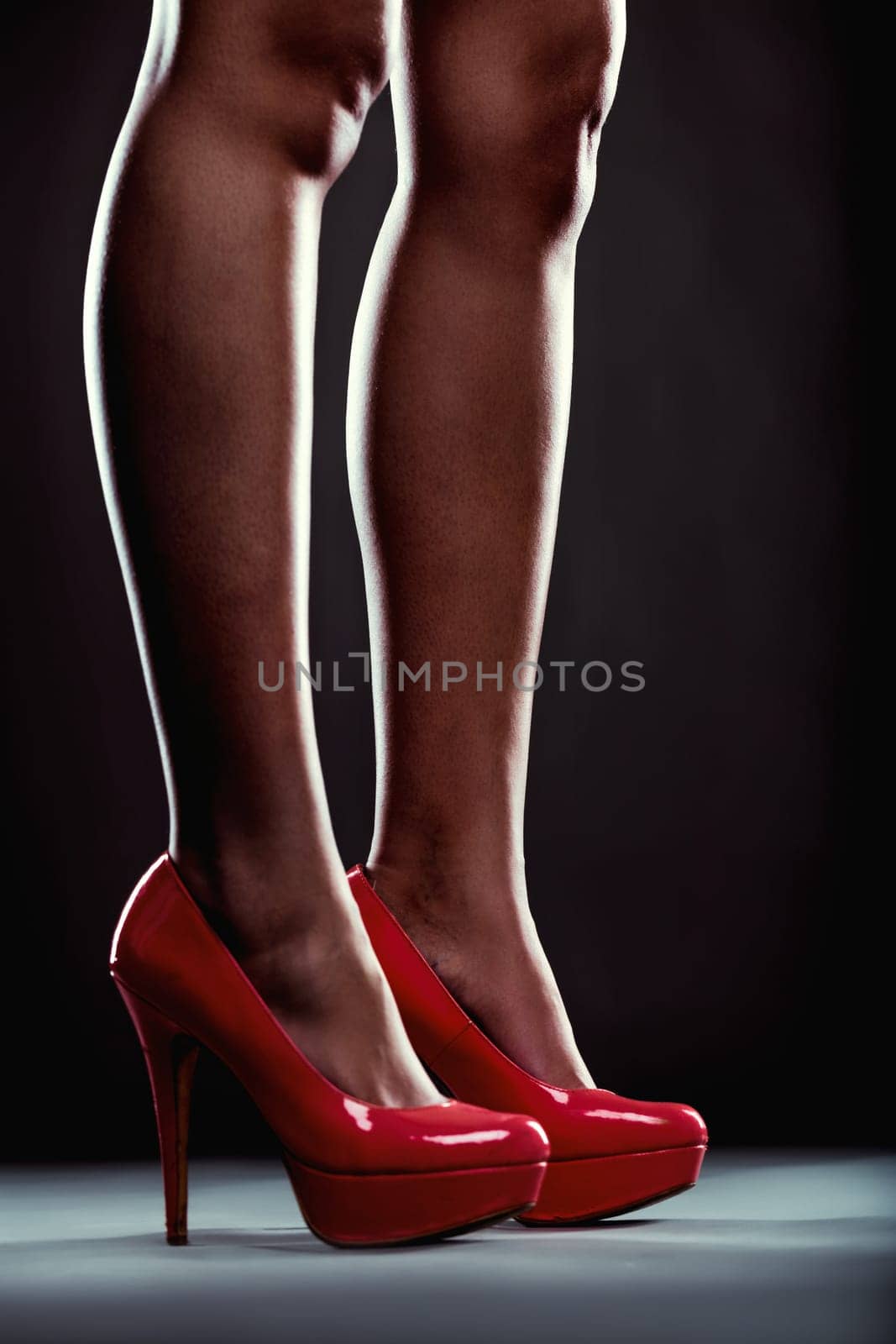 Close-up of a woman's legs wearing stylish, red high-heeled shoes, standing on a gray background, creating a sense of elegance and confidence