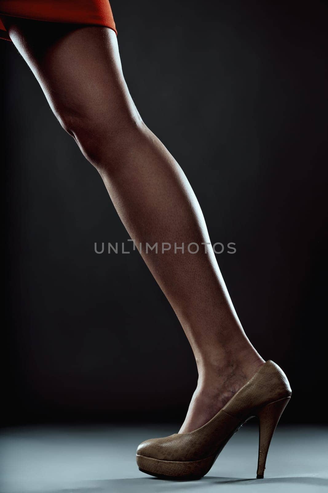 Close-up of a woman's legs in a striking red skirt and stylish high heels, stepping gracefully against a dark background, exuding elegance and modern fashion