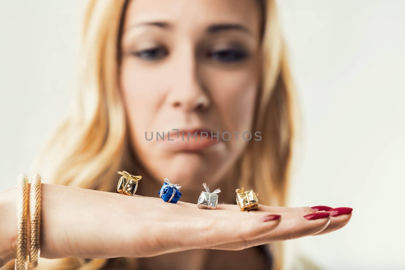 Blond woman showing disappointment while holding small wrapped gift packages in her hand, expressing lack of enthusiasm and negative feelings about receiving insignificant presents
