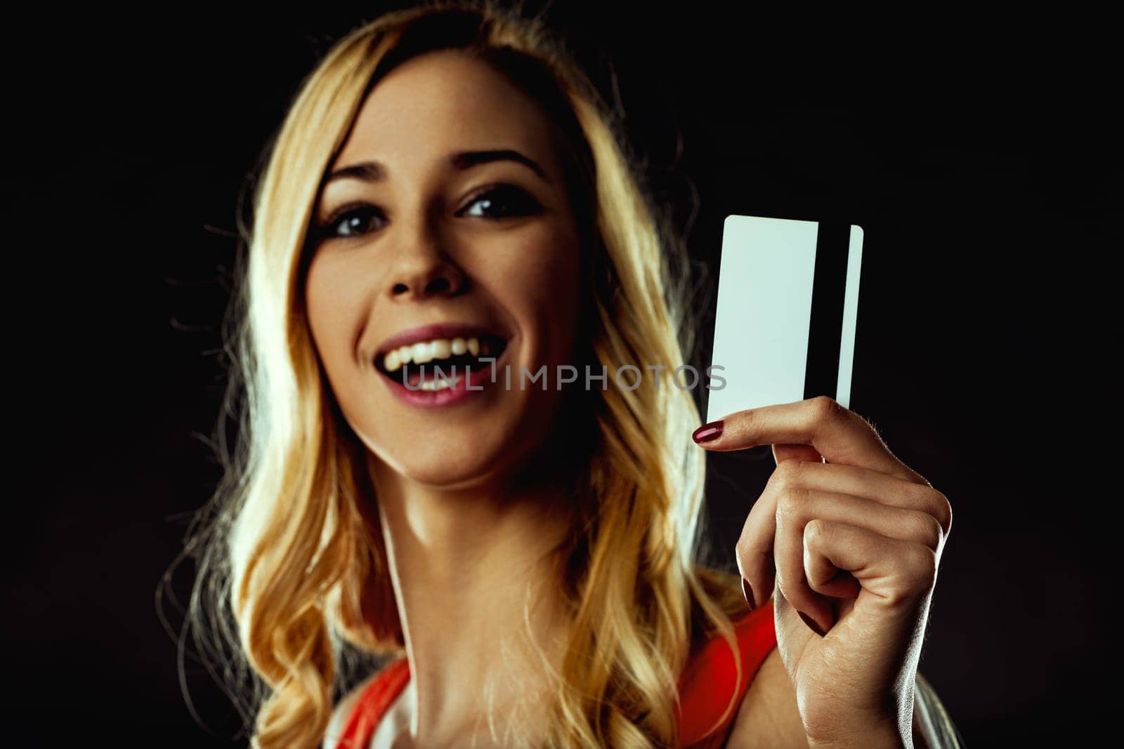 Excited young woman showing a generic credit card with a magnetic stripe and blank space for adding design or text, on a dark background
