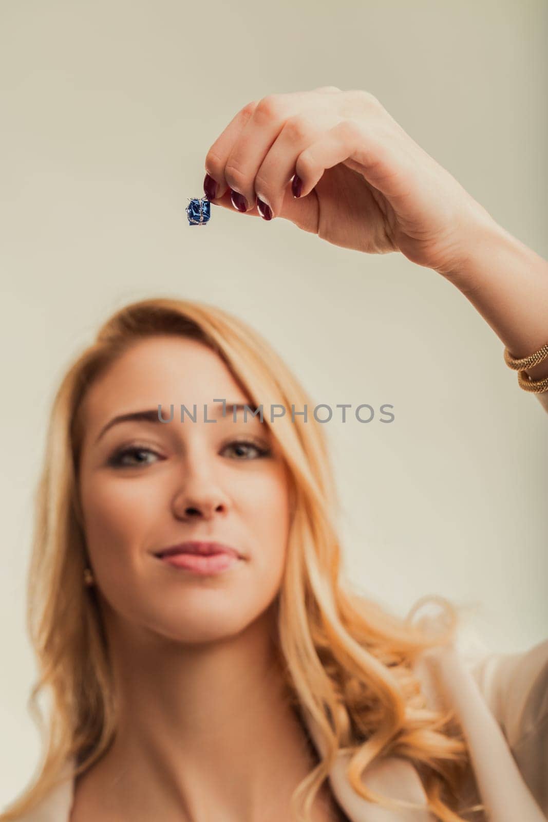 Young blonde woman holding a small gift box between her fingers, representing emotions, feelings and related concepts, in a studio shot with a neutral background