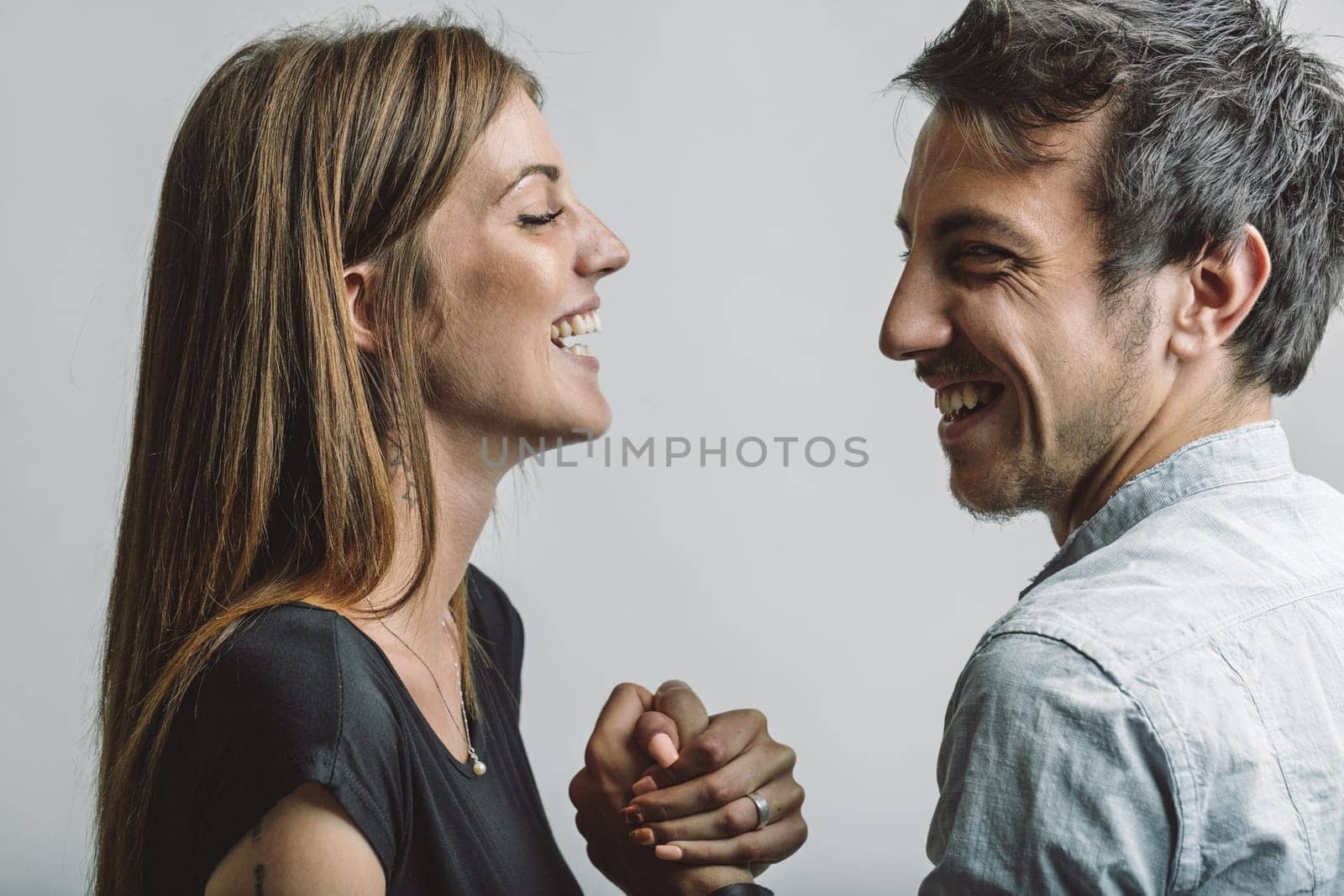 Studio shot featuring a young couple smiling and holding hands, radiating affection and complicity while enjoying a moment of joy and connection against a clean white background
