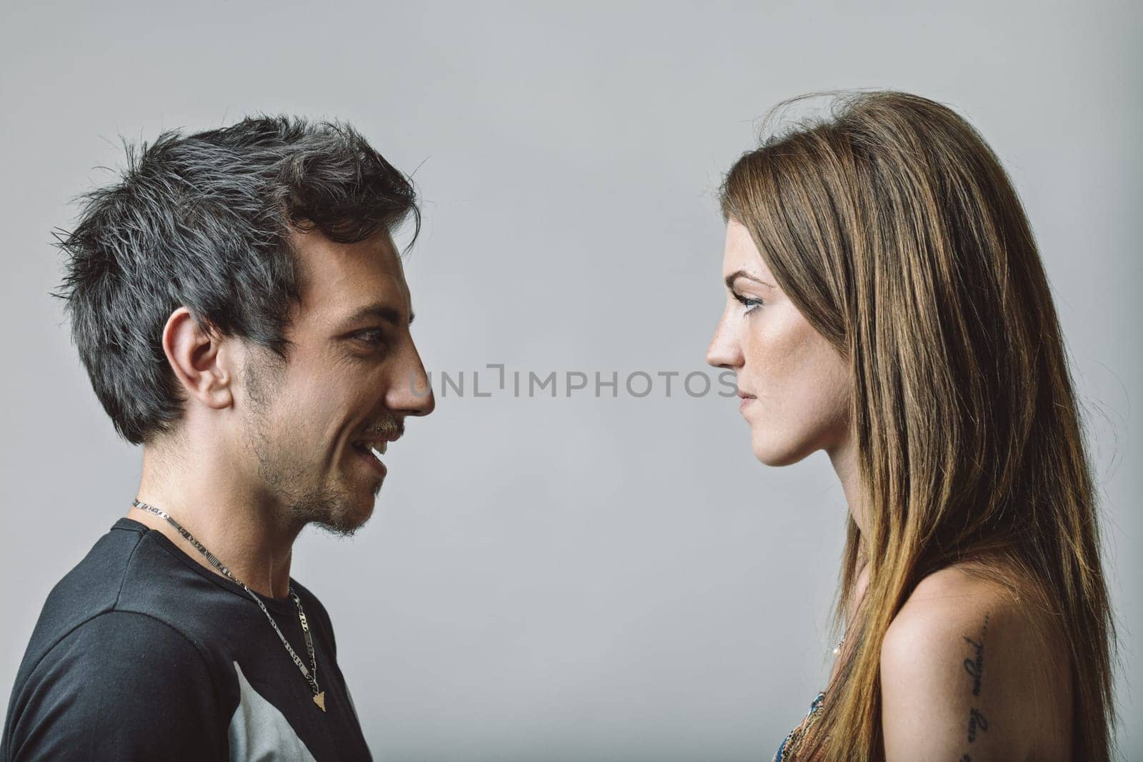 Profile of a young couple engaging in a face-to-face discussion, with the man smiling and the woman displaying a serious expression, capturing the tension of their relationship