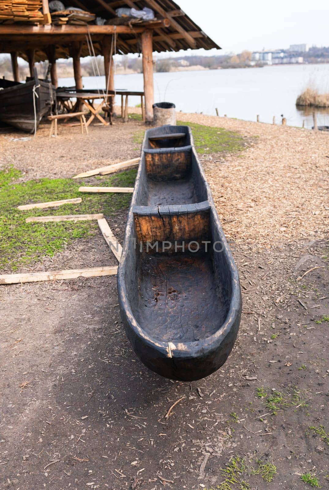 A handcrafted dugout canoe displayed near a lakeside workshop, showcasing traditional wooden craftsmanship.