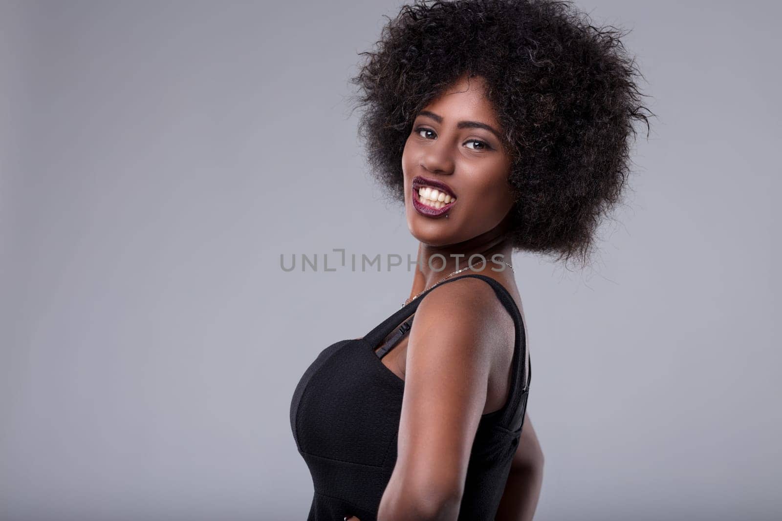 Studio portrait of a cheerful young african american woman with an afro hairstyle, wearing a black top, looking at the camera with a playful smile, expressing confidence and happiness